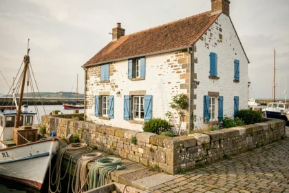 Petite maison de pêcheur en pierre blanche avec volets bleus au bord d'un port breton en France